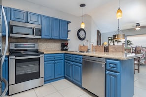 A kitchen with blue cabinets, stainless steel appliances, a granite countertop, and pendant lighting.