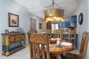 A dining area with a round wooden table, chairs, a colorful cabinet, and a kitchen in the background.