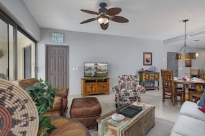 A spacious living room with a ceiling fan, a television, and a dining area with wooden furniture.