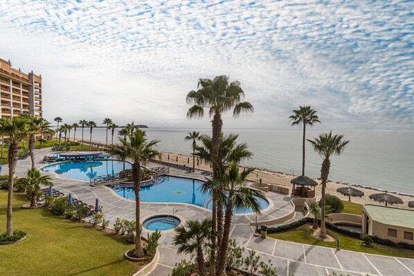A resort with a large pool, palm trees, and a view of the ocean.