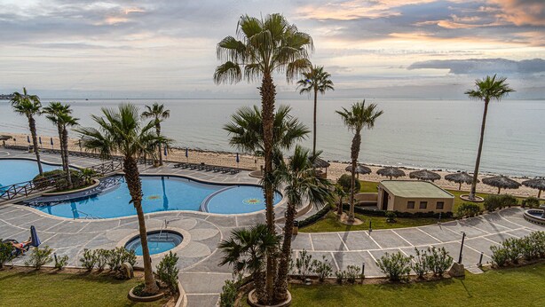 Un resort con una gran piscina, palmeras y vista a la playa.