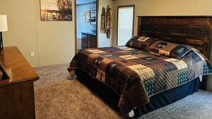 A bedroom with a wooden headboard, a large bed with a quilt, a nightstand, a lamp, and a painting on the wall. - Secluded Farm near Bennett Springs State Park, 66 Robin Ln Tunas, MO 65764 (Lebanon)
