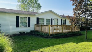 A single-story house with a front deck, a small garden, and a tree with autumn leaves. - Secluded Farm near Bennett Springs State Park, 66 Robin Ln Tunas, MO 65764 (Lebanon)