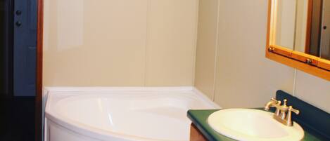 A bathroom with a white bathtub, a sink with a green countertop, wooden cabinets, and a mirror with lights above it.