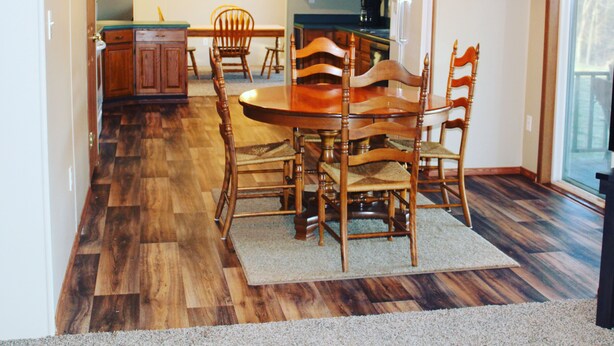 A dining area with a wooden table and chairs, a chandelier, and a kitchen in the background. - Secluded Farm near Bennett Springs State Park, 66 Robin Ln Tunas, MO 65764 (Lebanon)