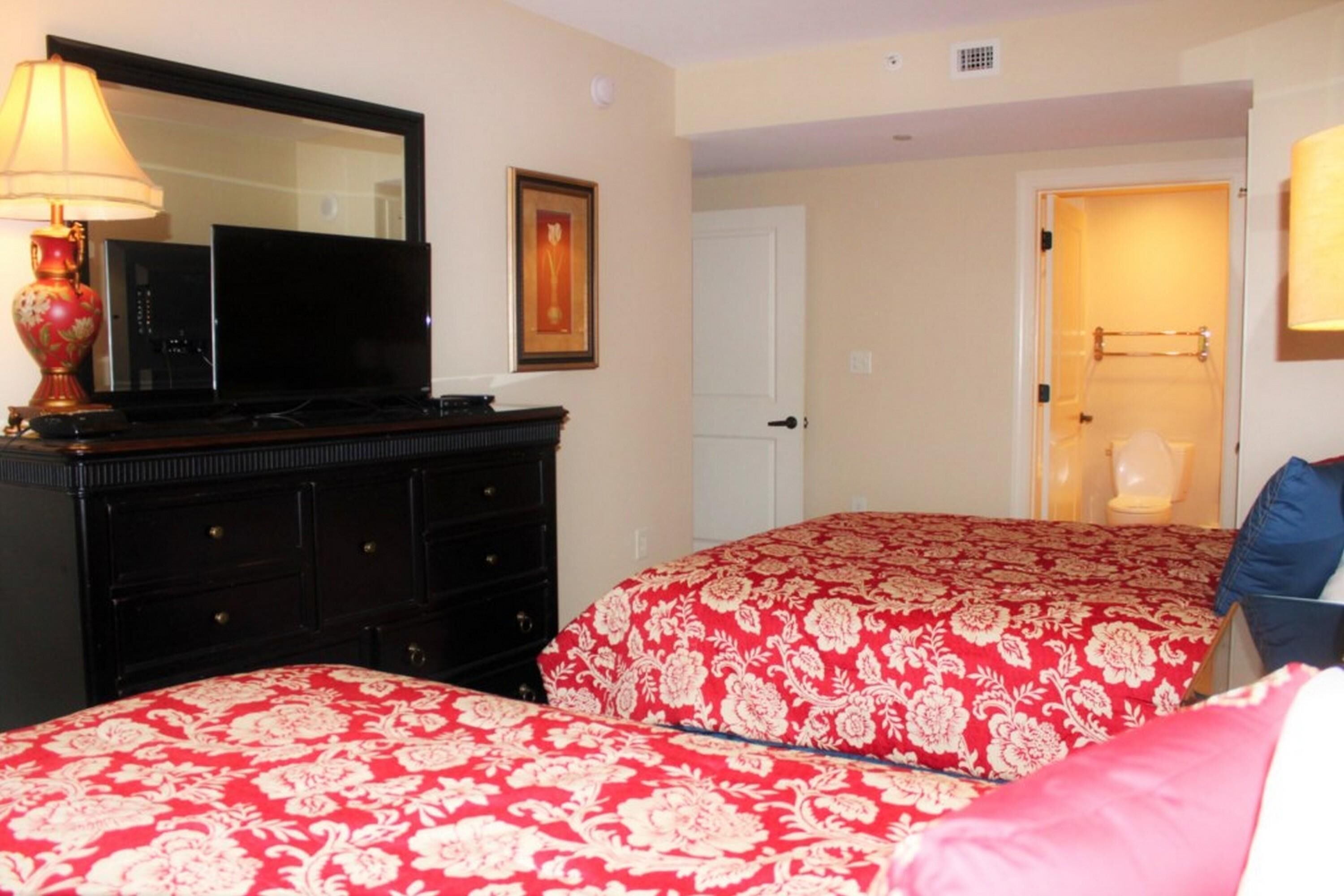 Una habitación de hotel con dos camas, un aparador, un televisor y una puerta que da a un baño.