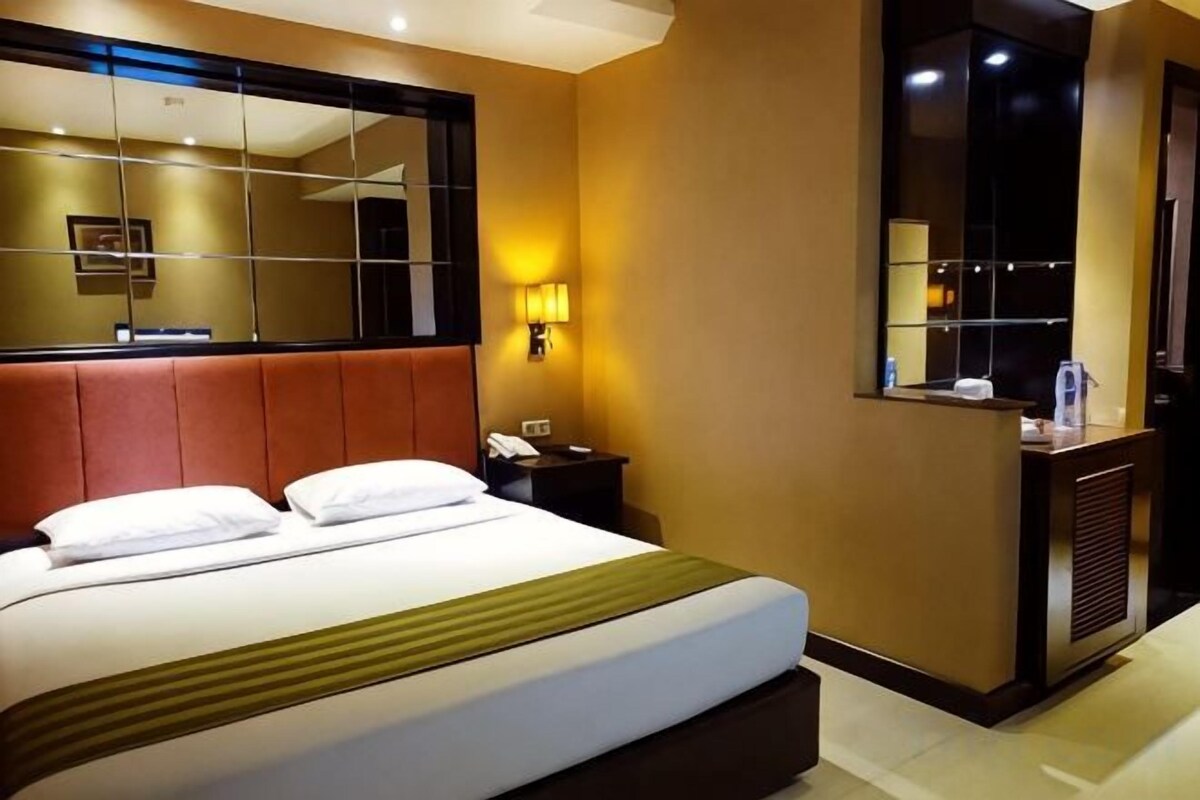 A hotel room with a large bed, a bedside table, a mirror, and a wall-mounted light.