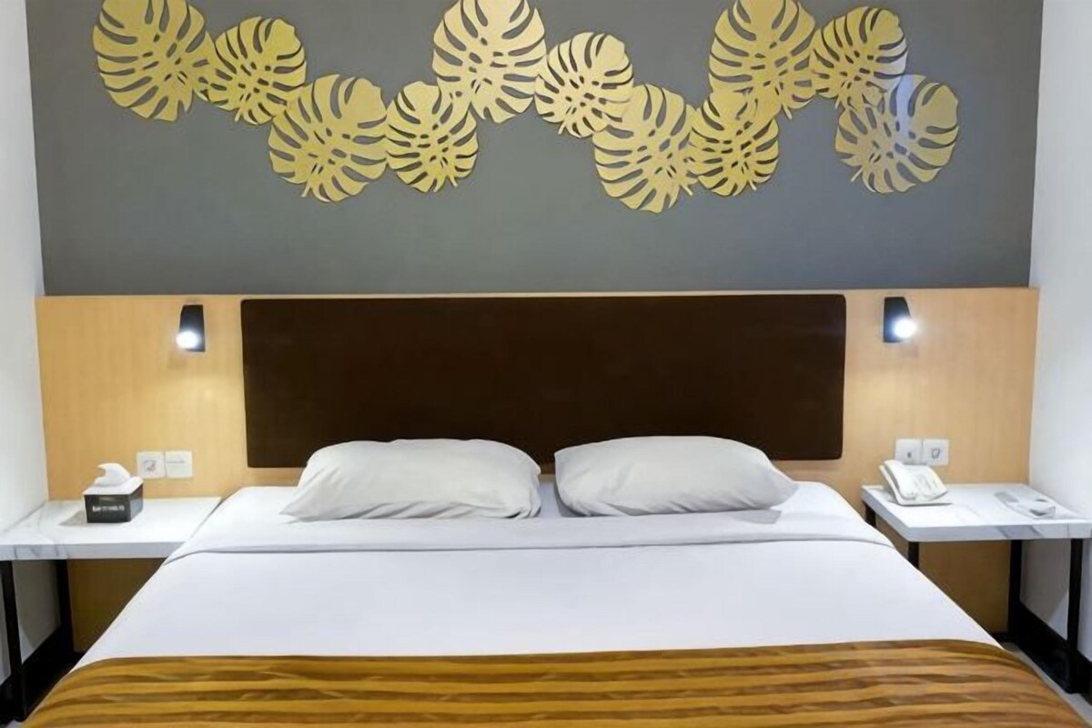 A hotel room with a bed, two bedside tables, a headboard, and a wall decoration.