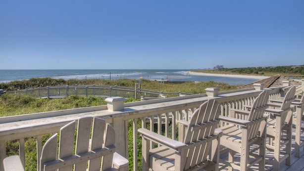 A beachside promenade with wooden chairs and a railing overlooking the ocean. - Ocean Creek Resort by Palmetto Vacations (Myrtle Beach)