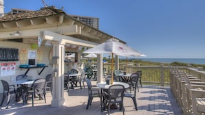 A seaside restaurant with outdoor seating, a terrace, and a view of the ocean. - Ocean Creek Resort by Palmetto Vacations (Myrtle Beach)