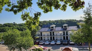 A building with solar panels on the roof, a parking lot with several cars, and a view of a green landscape.