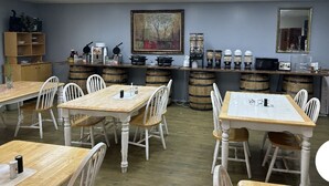 A dining area with wooden tables and chairs, a bar area with stools, and a large painting on the wall.