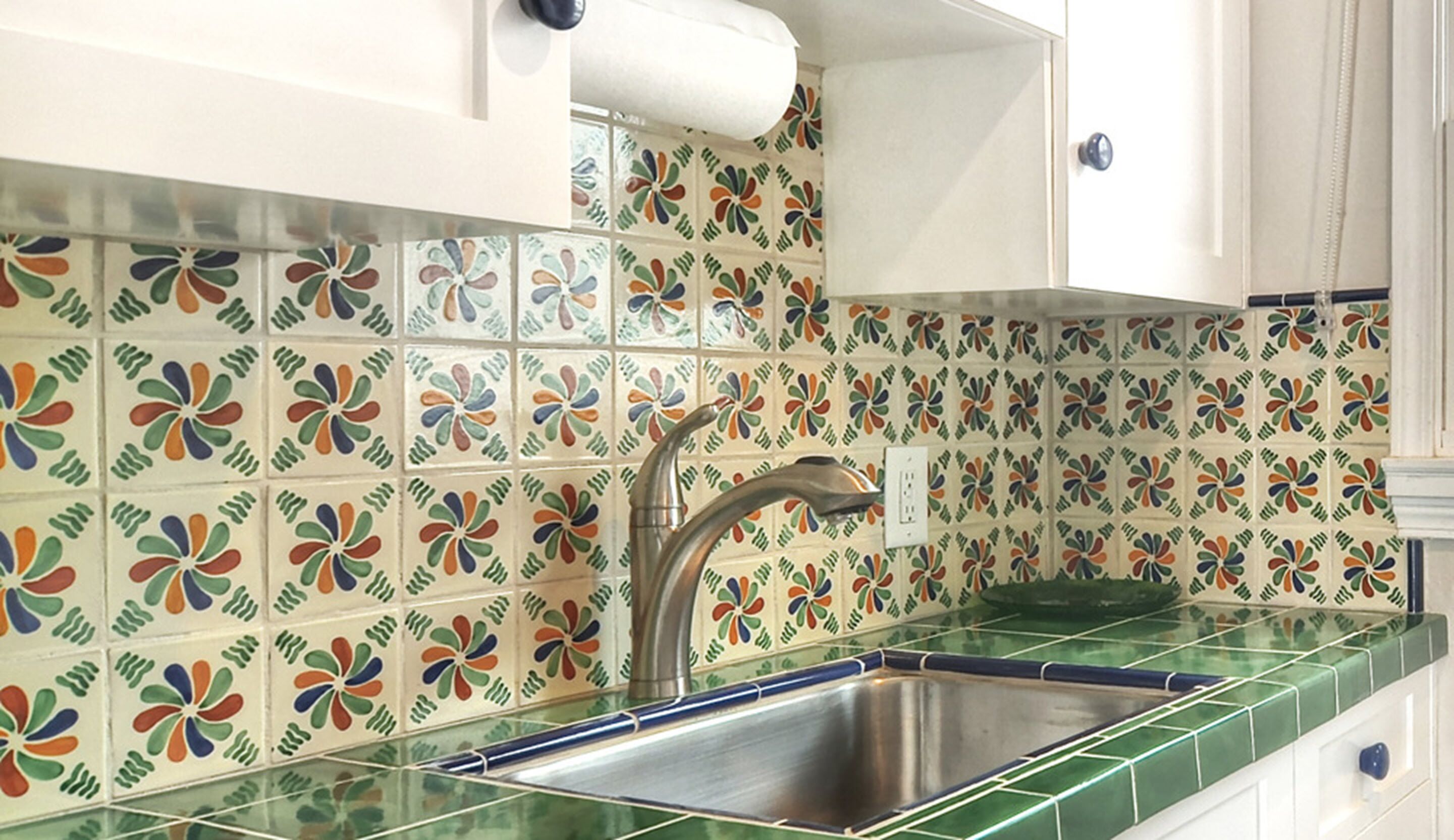 Una cocina con baldosas de flores coloridas, un lavamanos de acero inoxidable y armarios blancos.