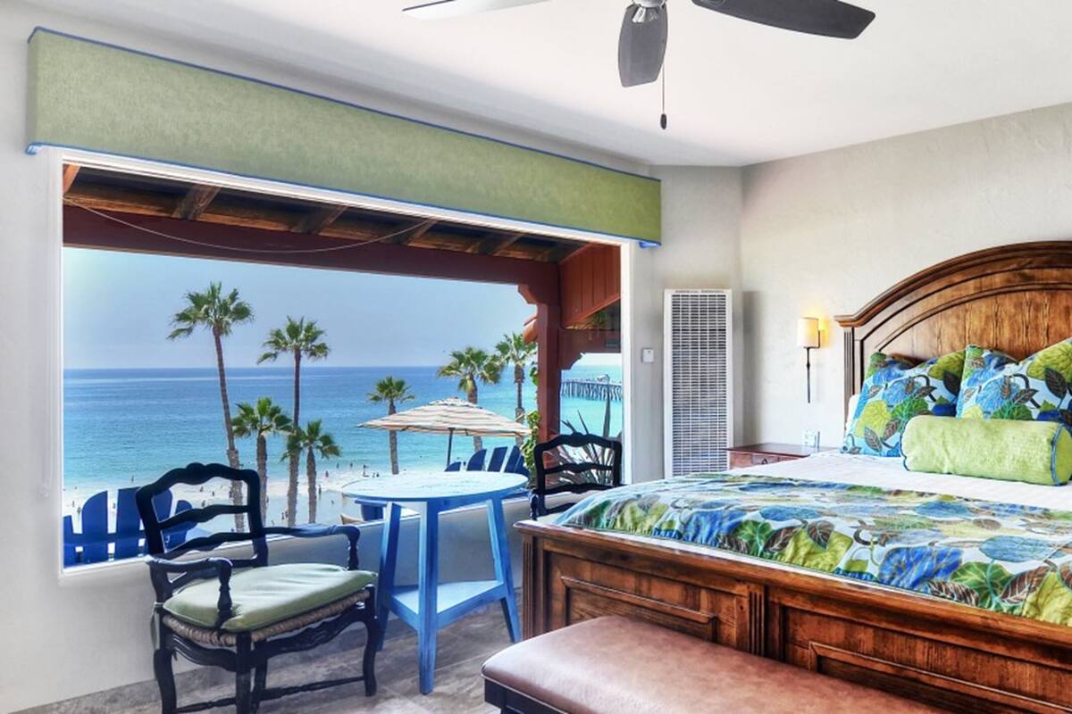 A bedroom with a large bed, a view of the ocean, a ceiling fan, and a window with a view of palm trees.