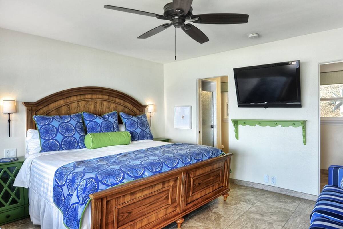 A bedroom with a wooden bed, a ceiling fan, a mounted TV, and a green chair.