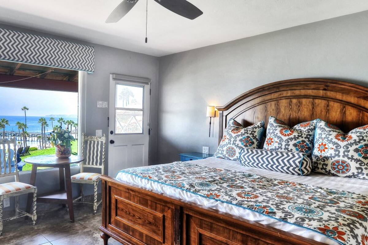 A bedroom with a large bed, a view of the beach, and a balcony with a table and chairs.