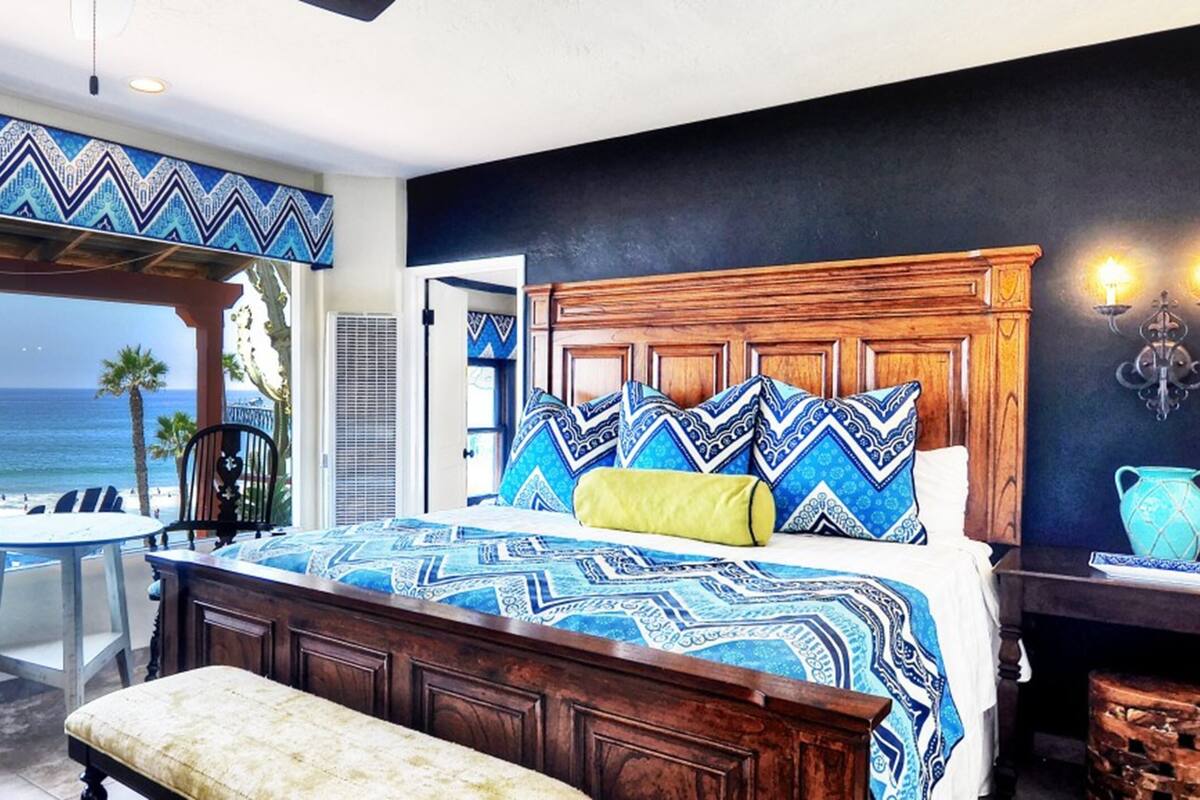 A bedroom with a wooden bed, a view of the beach, a small table, and a chair.
