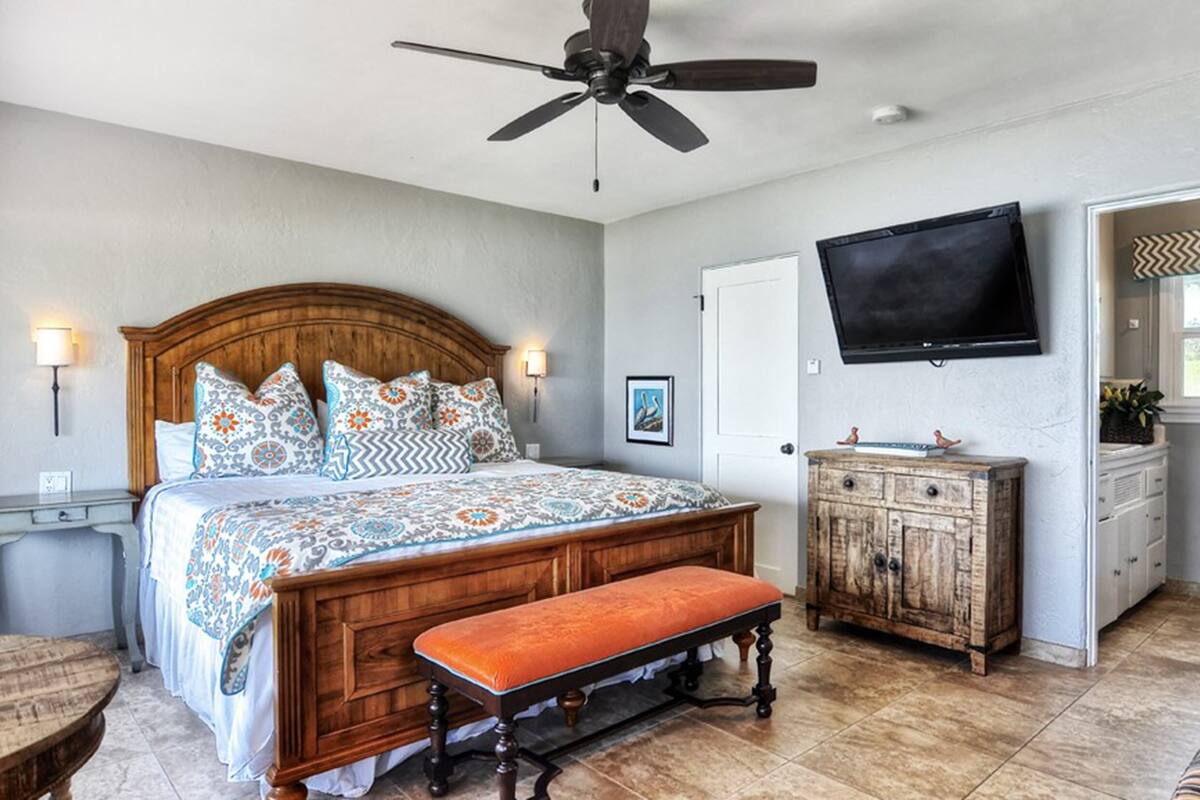 A bedroom with a wooden bed, a bench, a wooden cabinet, a television, and a window.