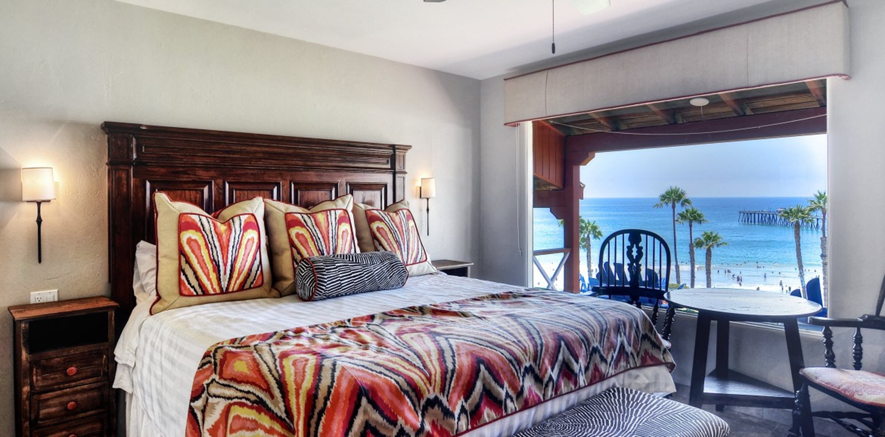 Een slaapkamer met een groot bed, uitzicht op het strand, een klein tafeltje en een stoel.