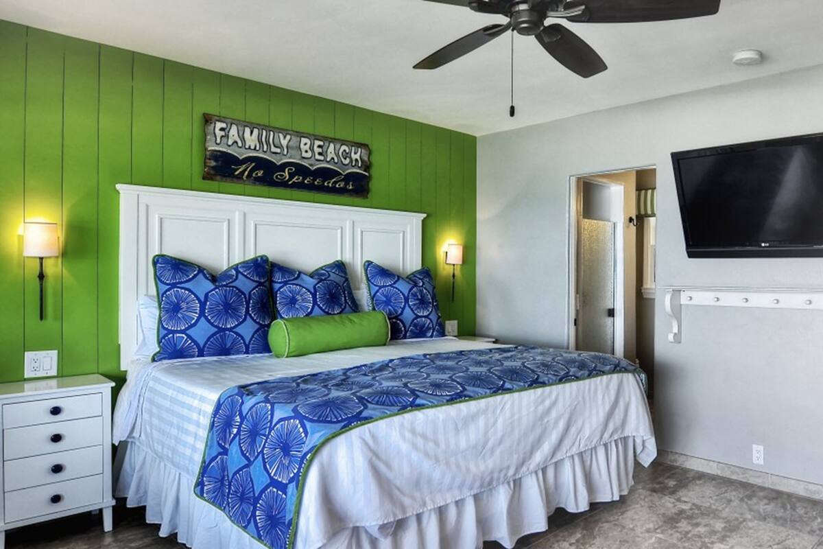 A bedroom with a bed, a television, a nightstand, and a green accent wall.