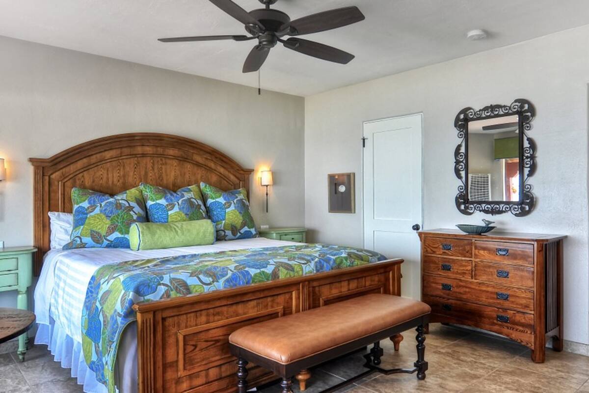A bedroom with a wooden bed, a bench, a dresser, a mirror, and a ceiling fan.