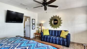 A hotel room with a bed, a sofa, a ceiling fan, a flat-screen TV, a microwave, and a decorative mirror.