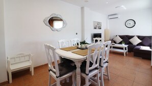 A dining area with a white table and chairs, a white bench, a sofa, and a wall clock. - 1155 Apartment SanJuan 18 (Nerja)