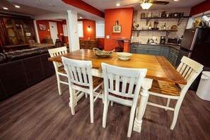 Uma sala de jantar com mesa de madeira e cadeiras brancas, uma cozinha com paredes vermelhas e eletrodomésticos modernos, e um espaço bar com mobiliário de madeira escura.