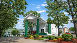 A building with a white facade and green columns, surrounded by trees and a well-maintained garden.