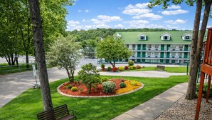 A well-maintained lawn with a bench, a tree, and a building with a green roof in the background.