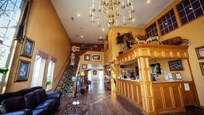 A spacious lobby with a grand chandelier, a reception desk, and a staircase leading to an upper level.