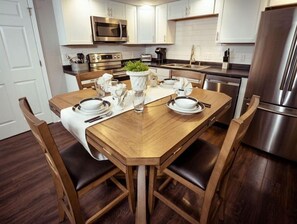 Cozinha moderna com armários brancos, eletrodomésticos de aço inoxidável e uma mesa de jantar de madeira para quatro pessoas.