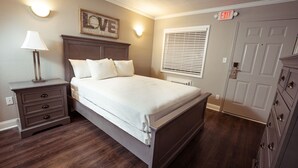 A bedroom with a bed, nightstand, dresser, and an exit sign.