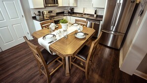 A modern kitchen with white cabinets, stainless steel appliances, and a wooden dining table set for four.