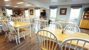 A dining area with wooden tables and white chairs, a television, and a bookshelf.