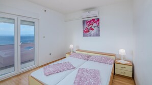 Une chambre à coucher comprenant un lit, deux tables de chevet, une commode, une fenêtre donnant sur la mer et un appareil de climatisation.