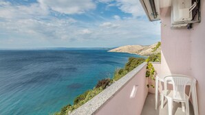 Un balcon avec vue sur la mer, une chaise blanche et un immeuble avec un mur rose.