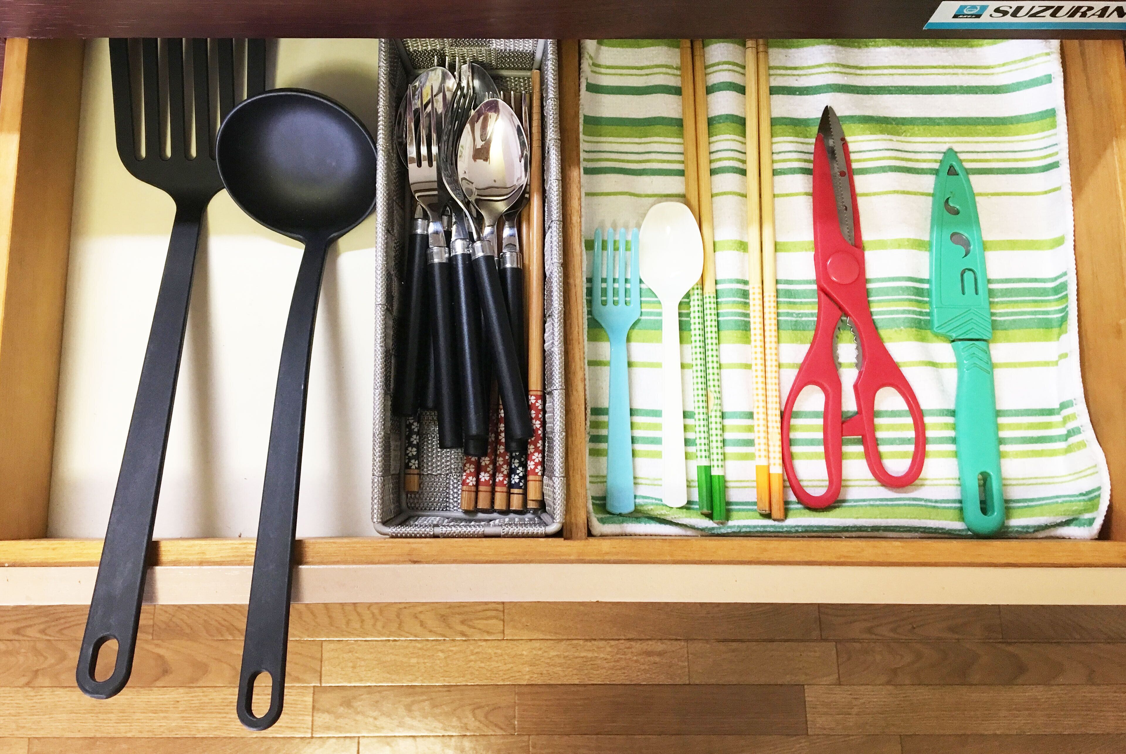 Un cajón con varios utensilios de cocina, incluyendo una cuchara de lacaje negra, cucharas, un tenedor azul, una espátula roja y un cuchillo verde.