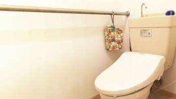 A toilet with a white lid, a wall-mounted handrail, and a small hanging bag with a fruit pattern.