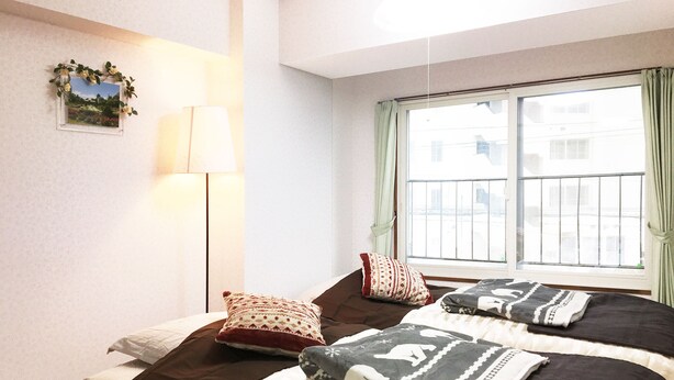 A bedroom with two beds, a window with curtains, a wall-mounted lamp, and a framed picture. - Sapporo-ENJU Nakanoshima 204 (Sapporo)