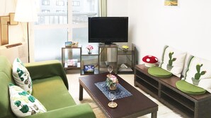 A living room with a green sofa, a coffee table with a vase and wine glass, a TV, and a cactus-themed bench. - Sapporo-ENJU Nakanoshima 204 (Sapporo)