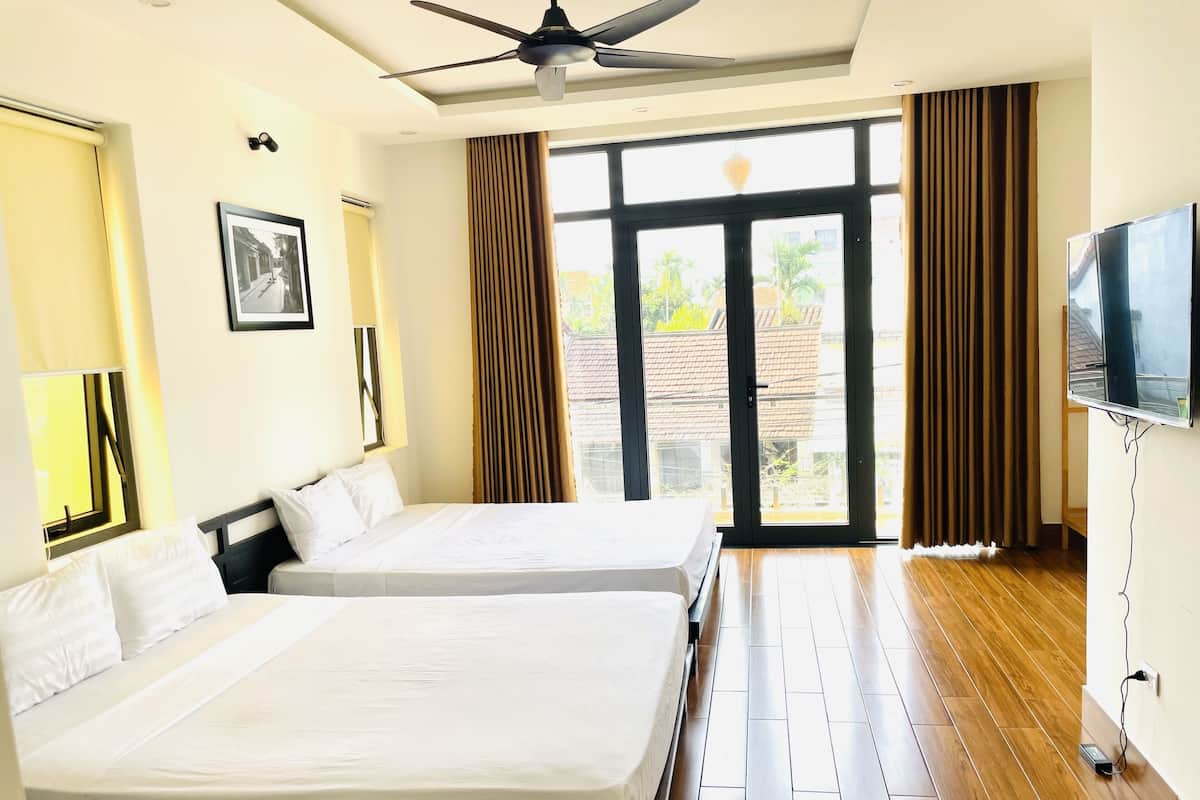 A hotel room with two beds, a ceiling fan, a TV, and a large window with curtains.