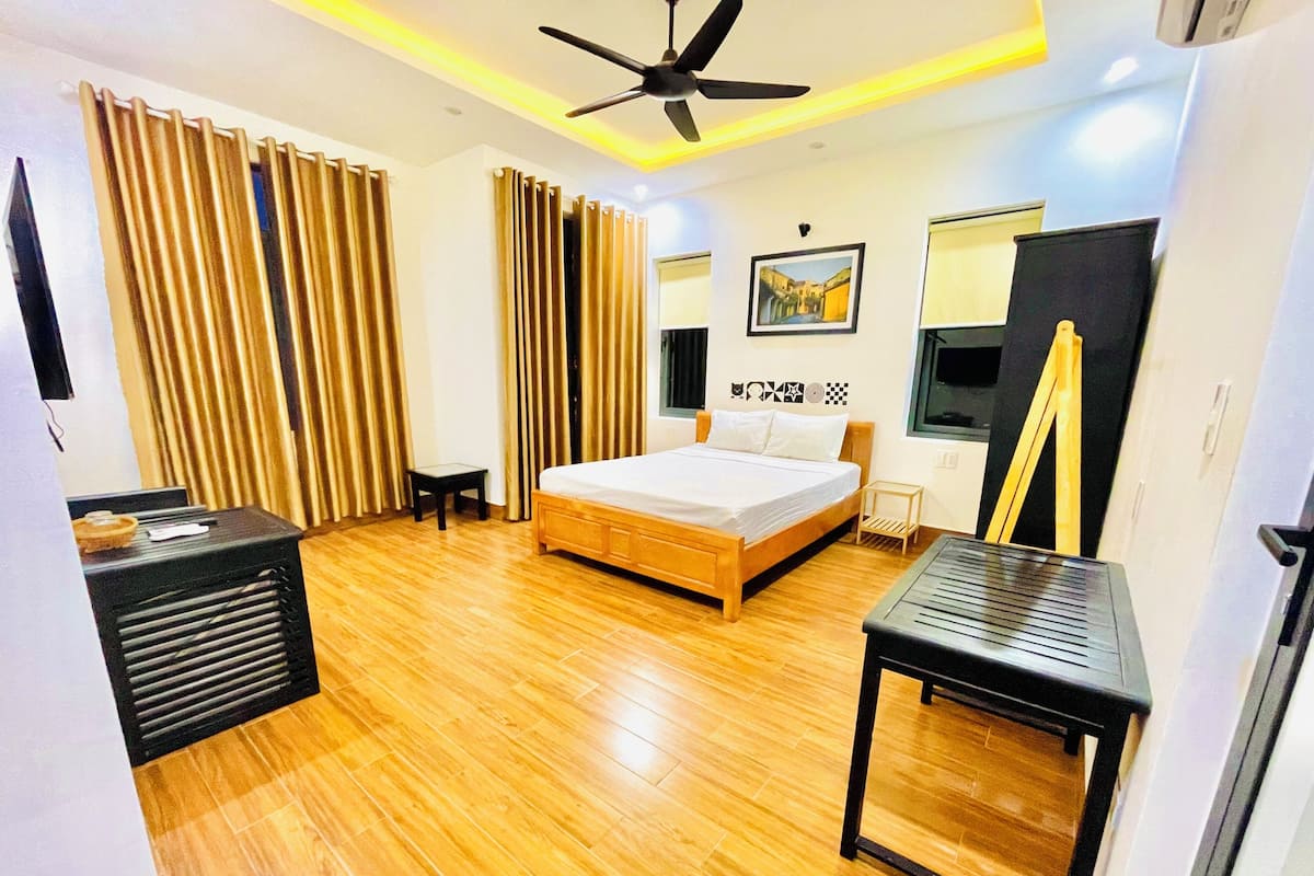 A modern hotel room with a wooden floor, a bed with white linens, a ceiling fan, a painting on the wall, and a small table.