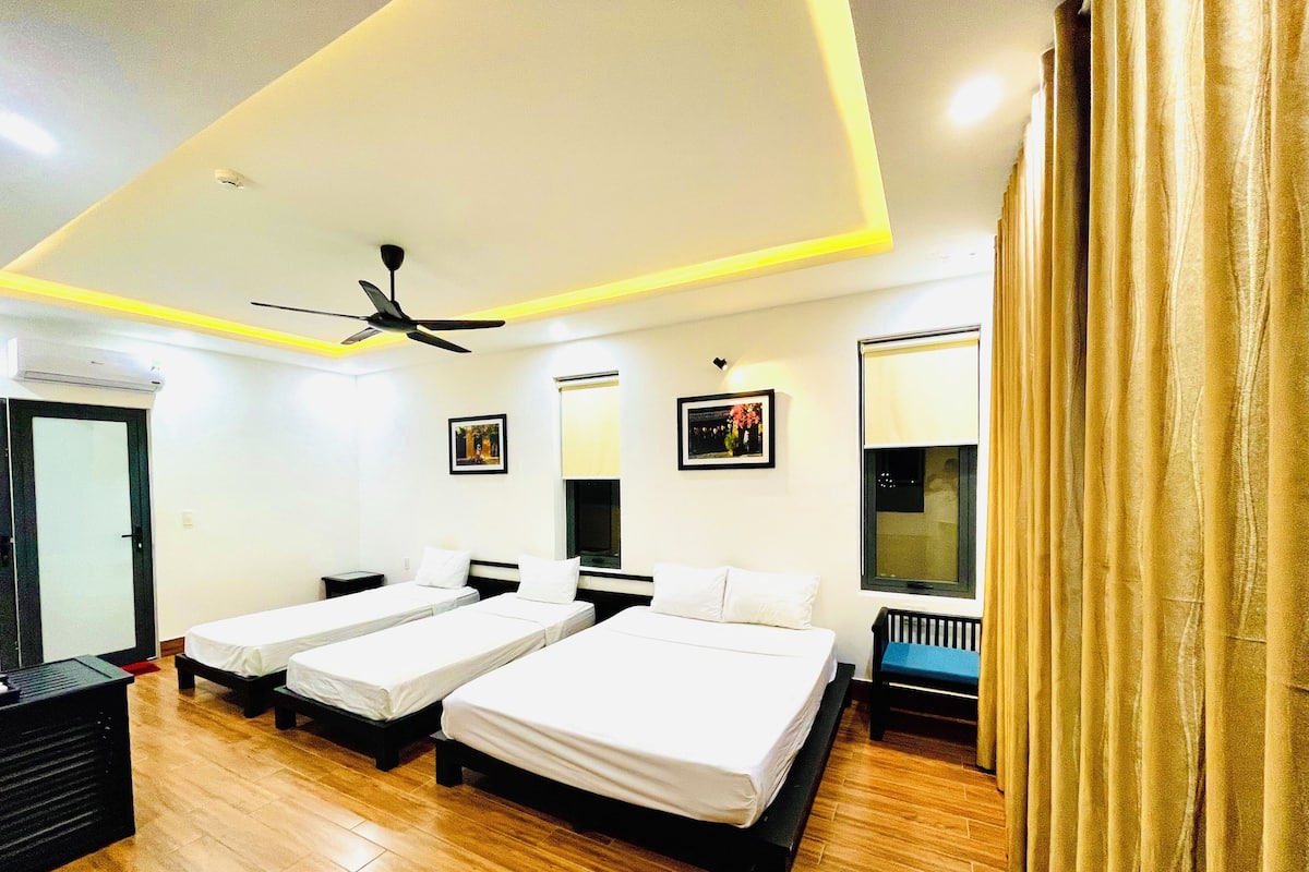 A hotel room with two single beds, a ceiling fan, a window with blinds, and a door.