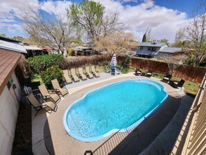 A swimming pool with lounge chairs and a small table, surrounded by a wooden deck and a wooden fence. - Lake Powell Home with Pool (Page)