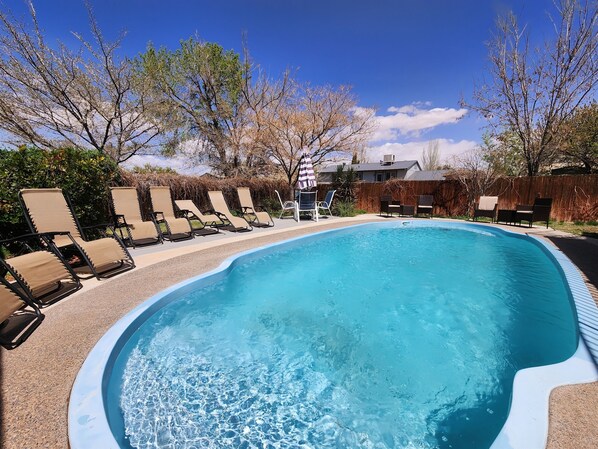 A swimming pool with lounge chairs and a wooden fence in the background. - Lake Powell Home with Pool (Page)