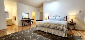 A hotel room with a bed, a desk, a chair, a mirror, and a small table with a lamp. - Lake Powell Home with Pool (Page)