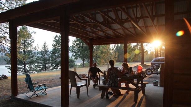 A covered outdoor seating area with a view of a lake and trees.