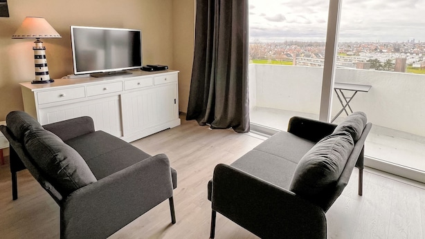 Una sala de estar moderna con un televisor de pantalla plana, una mesita, dos sofás y un balcón con vista a la ciudad.