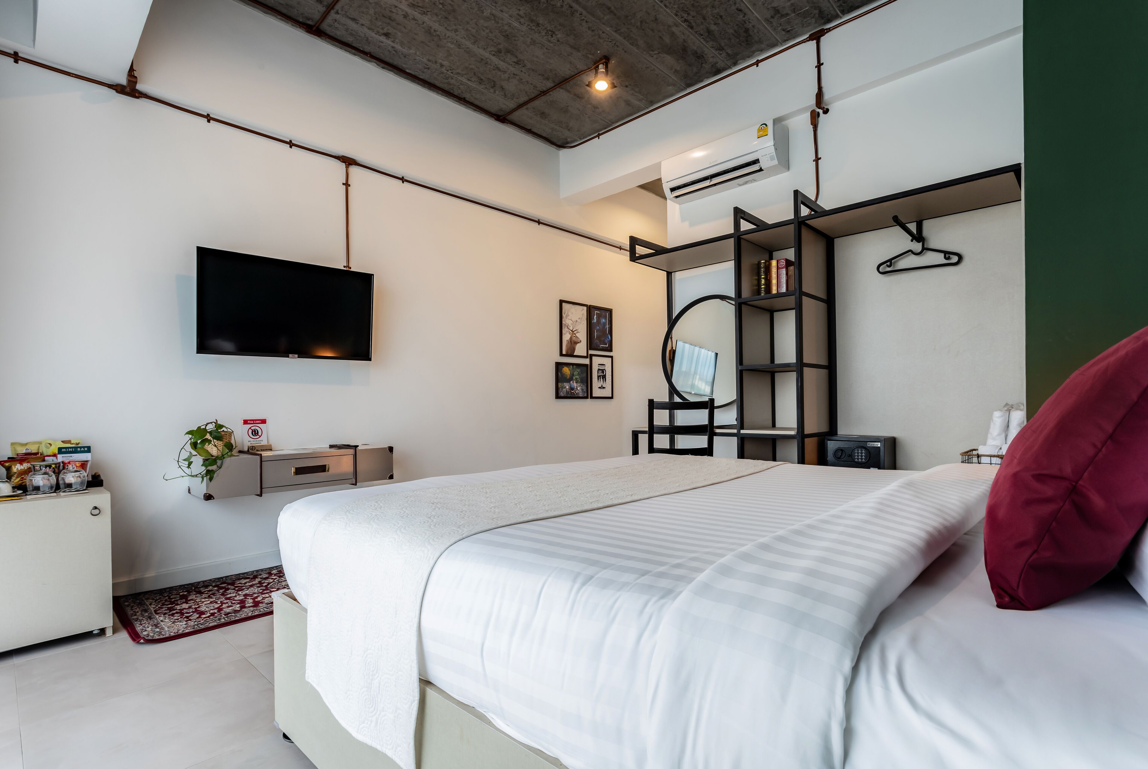 A modern bedroom with a large bed, a mounted TV, a desk with a chair, a bookshelf, and a hanging coat rack.